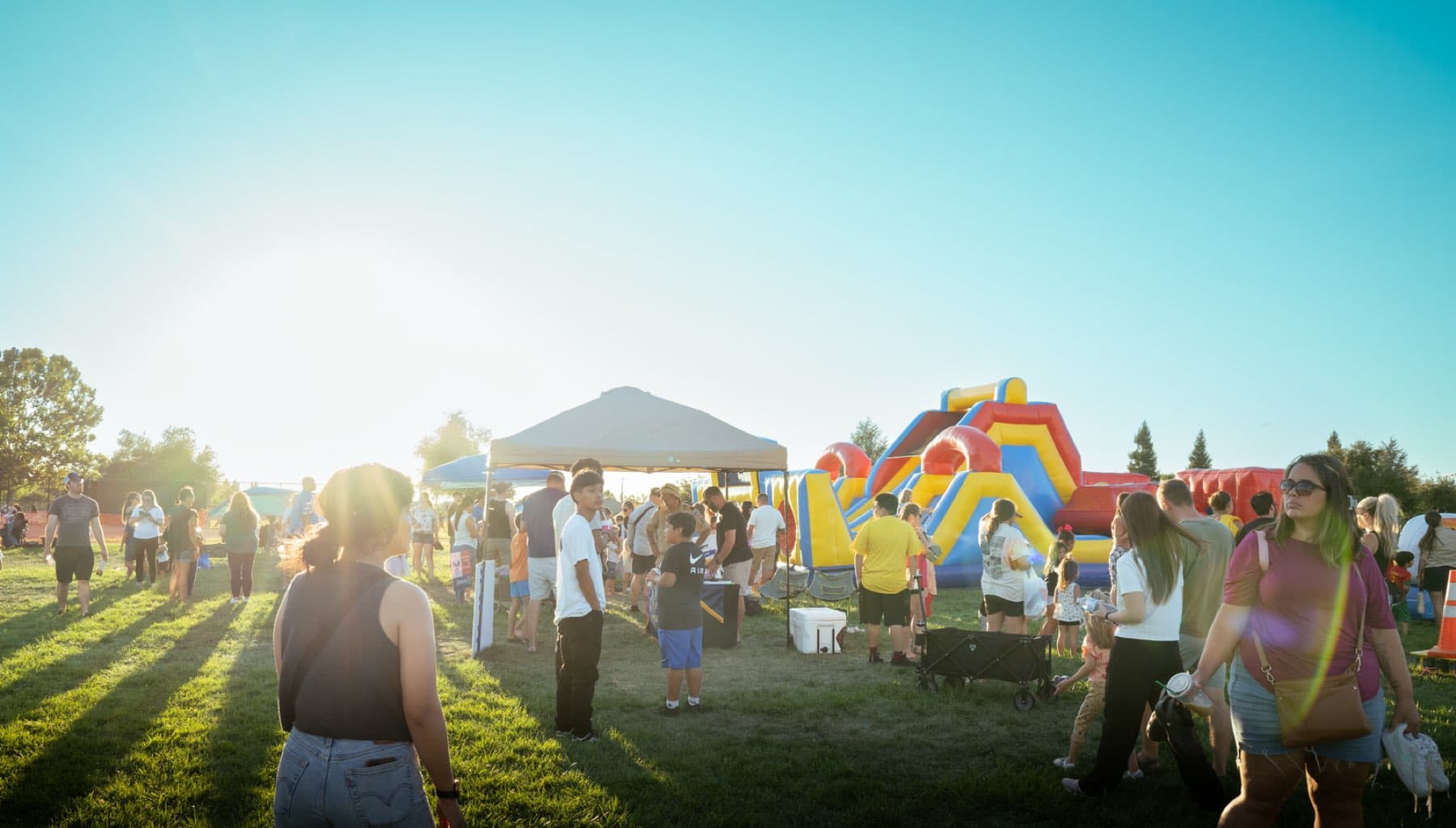 Families walking between pop-up vendor tents and inflatables at an outdoor community event